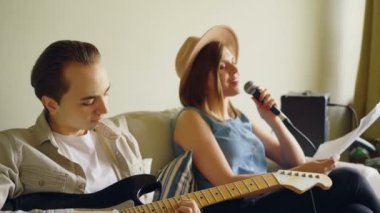 Yaratıcı müzik düet evde pratik kadın mikrofon şarkı söylemek ve adam gitar çalıyor. Neşeli gençler rahat kıyafetler giymiş.