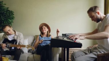 Yaratıcı genç insanlar müzisyenler şarkı ve müzik aletleri klavye ve gitar çalmaya evde prova. İç ve müzikal ekipman görünür.
