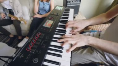 Sakallı genç arkadaşları şarkı ve prova sırasında evde kanepede oturup gitar çalmak klavyeci klavye oynuyor. Erkek el üstünde anahtar düğme yakın çekim.
