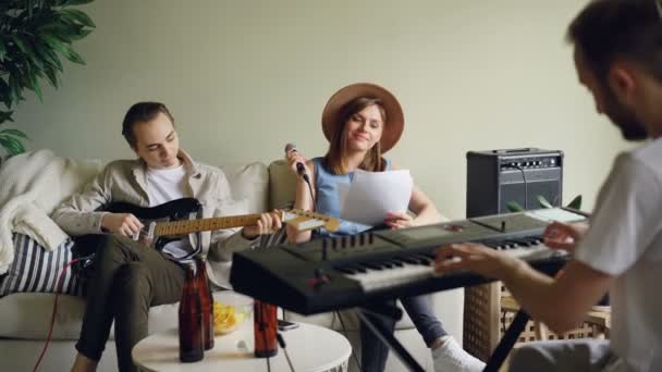 Aantrekkelijke jonge mensen muzikale band houden repetitie op kamer thuis, spelende muziekinstrumenten en het zingen in de microfoon. Muziek en millennials concept. — Stockvideo