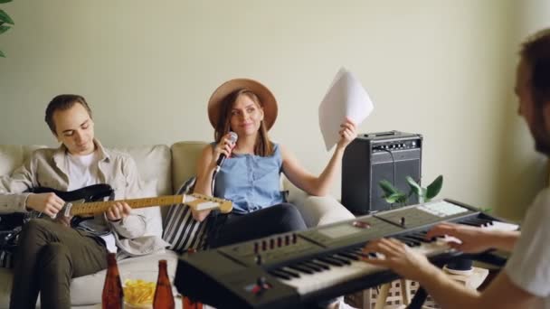 Fröhliche junge Leute üben im heimischen Studio Gesang und spielen Keyboard und Gitarre. Musiker tragen lässige Kleidung. — Stockvideo