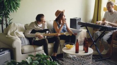 Müzikal grup performans şarkı ve müzik aletleri müzik sayfasına bakarak ev stüdyosu oynamaya prova yapıyor. Şişe ve tablo snacks görülebilir.