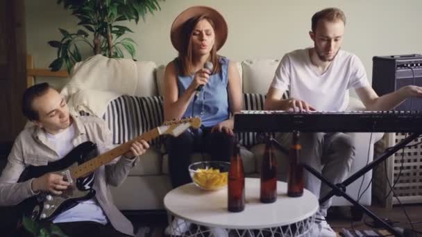 Mooie blonde zanger is zingen en magnetisch vingers terwijl haar vrienden en collega's uit de muzikale band speelt het toetsenbord en de elektrische gitaar. — Stockvideo