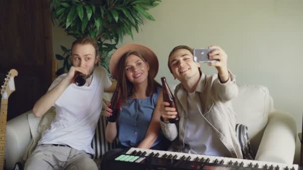 Músicos amigos felizes em roupas casuais estão tomando selfie segurando garrafas e bebendo cerveja. alegres millennials estão posando e rindo se divertindo no estúdio . — Vídeo de Stock