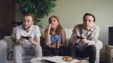 İki erkek arkadaş video sarışın kız oyunu izlerken ve abur cubur yeme joystick düğmelere basarak oyun mu oynuyorsun. Dostluk ve teknoloji kavramı.