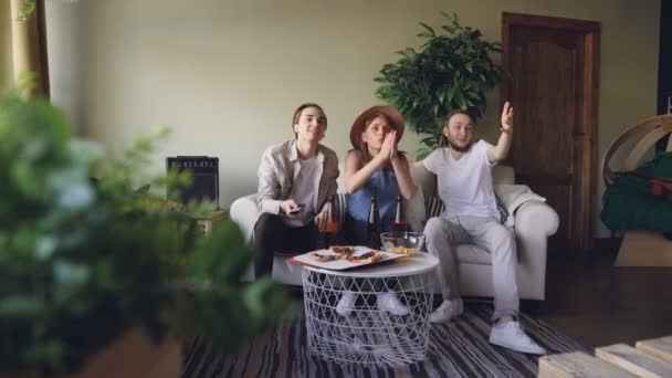 Emocionados fanáticos de los deportes están viendo juegos en la televisión en casa juntos y animando emocionalmente luego celebrando la victoria con los cinco altos y saltando sobre los pies . — Vídeo de stock