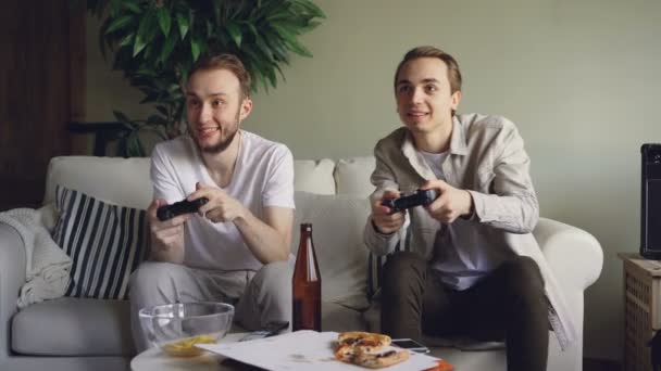 Careless studenter spelar videospel titta på skärmen och trycka på joysticksknappar, en är att förlora en är vinnande och glad. Vänskap och teknik koncept. — Stockvideo