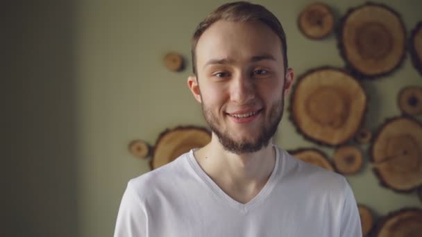 Al rallentatore del bel ragazzo barbuto che indossa una maglietta bianca guardando la telecamera, sorridendo e ridendo. Persone attraenti e concetto di felicità . — Video Stock