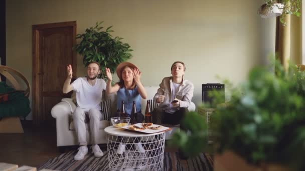 Mouvement lent des personnes actives fans de sport regarder le jeu à la maison sur le canapé puis sauter sur les pieds et faire cinq hauts pour célébrer la victoire, fille lance chapeau . — Video