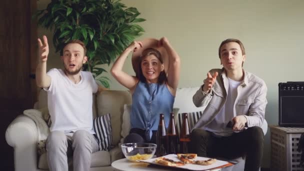 Cámara lenta de los fanáticos de los deportes nerviosos viendo el partido en casa en el sofá y luego saltar sobre los pies y haciendo cinco para celebrar la victoria, chica feliz está lanzando sombrero . — Vídeos de Stock