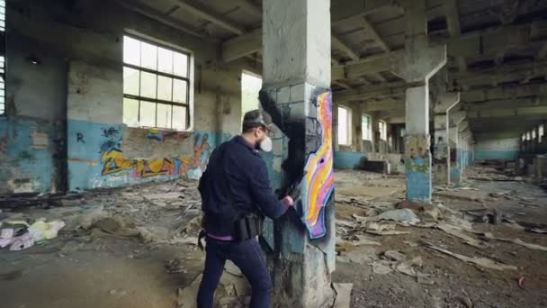 Foto Pan di uomo adulto graffiti artista in maschera protettiva e guanti pittura su pilastro alto all'interno danneggiato edificio industriale vuoto. Creatività e concetto di persone . — Video Stock