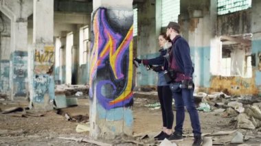 Kentsel ressam için çekici genç kadın nasıl grafiti boya için açıklayan, ayağı olarak hasarlı boş ambar holding sprey boya ve konuşurken yanında duruyorlar.