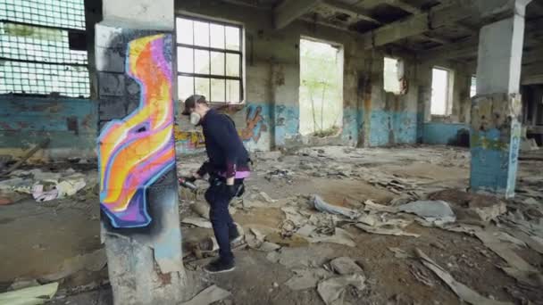 Joven pintor de graffiti profesional está trabajando dentro de un edificio abandonado, está pintando con aerosol en aerosol sobre una columna alta. Arte moderno y concepto de creatividad . — Vídeos de Stock