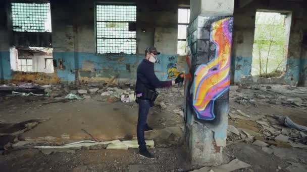 Mužské graffiti umělec je zdobení Staré poškozené sloupce uvnitř prázdné průmyslové budovy s abstraktní obrázky. Moderní malíř používá barev ve spreji.