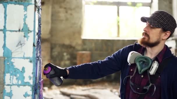 Attractive bearded guy is holding aerosol paint and drawing graffiti on pillar inside spacious abandoned house. Creative people, empty buildings and modern art concept. — Stock Video