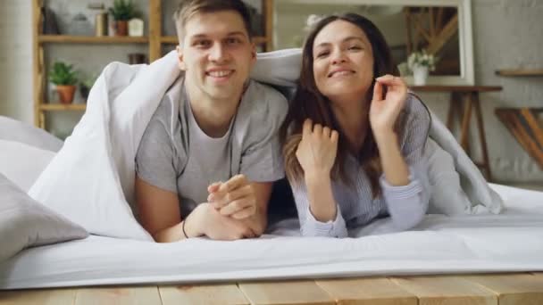 Портрет счастливой пары смешанной расы, выходящей из-под одеяла, улыбающейся и смотрящей в камеру. Счастливая семейная жизнь, привлекательные люди и концепция отношений . — стоковое видео