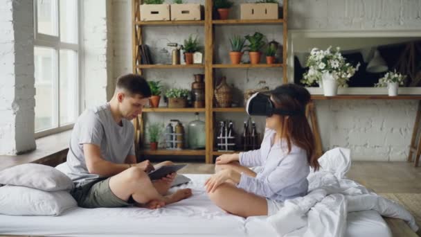 La pareja casada se está divirtiendo con gafas de realidad aumentada, la joven está usando entonces y sonriendo con las manos en movimiento y su marido está usando la tableta. Concepto de tecnología y personas . — Vídeos de Stock