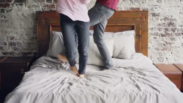 Amoureux heureux dansent sur le lit en se tenant la main et profiter de la vie conjugale ensemble. Moderne lit double, mur de briques et l'intérieur de l'appartement loft lumière est visible . — Video