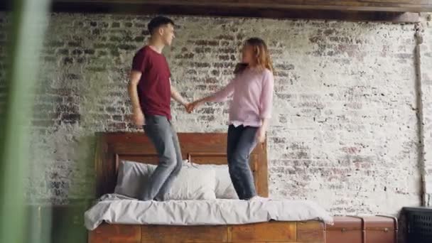 Joven novia y novio están bailando en la cama doble y besándose divirtiéndose juntos en el dormitorio. Gente activa feliz, relación romántica y concepto de amor . — Vídeos de Stock