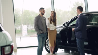 Çekici çift araba satış yöneticisi lüks araba bayilik'nde konuşma ve güzel siyah otomobil seyir. Lüks arabalar ve insanlar kavramı.