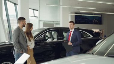 Araba Bayilik işçi güzel çift sakallı adam ve onun çekici karısı Lüks Araç Oto salonda yakın dururken konuşuyor. Yeni otomobil konsepti seçme.