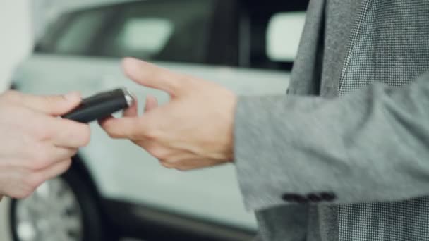 Primer plano plano de las manos que reciben las llaves del coche y estrechando la mano con el vendedor después de un acuerdo exitoso en sala de exposición de automóviles. Compra y venta de autos, hombres de negocios y concepto de apretón de manos . — Vídeo de stock