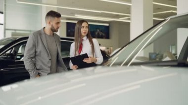 Çekici kadın araba satıcısı baktılar müşteriye yeni otomobil modeli hakkında konuşmak ve belgeleri duran güzel araba yakınındaki birlikte tutan.