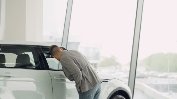 Selbstbewusste gutaussehende junge Mann schaut auf schöne Auto in Automobil-Showroom und berühren sie und zu Fuß durch Auto. Fahrzeug- und Personenkonzept. — Stockvideo