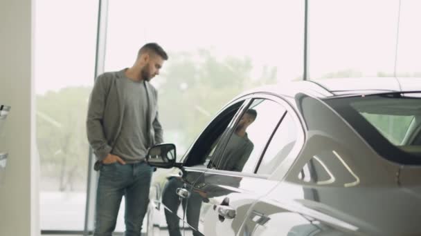 Interesse klant is mooie auto in motor showroom, inspecteren, kijken naar auto en aan te raken. Focus op glanzende nieuwe auto, mans reflectie is zichtbaar. — Stockvideo