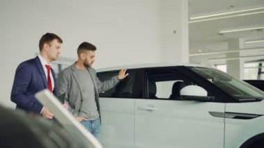 Ciddi adam araba satıcısı motor showroom yeni otomobil modeli, belgeleri holding salesmanis tartışmak için konuşuyor. Satın alma araç ve insan kavramı.