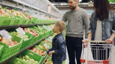 Genç aile anne, baba ve küçük çocuk meyve dokunmaktan ve onları kokulu ve arabası içinde koyarak süpermarkette tercih ediyor. Gıda ve insanlar kavramı için alışveriş.