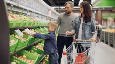 Genç çocuk ailesiyle yemek süpermarkette alışveriş, Anne meyve tercih ediyor ve çocuk onları alışveriş sepeti koyuyor. Bakkal ve aile hayat kavramı.