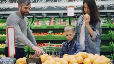 Mutlu aile portakal süpermarkette seçmektir, anne baba ve sevimli çocuk meyve, onları kokulu sonra alışveriş sepeti koyarak alıyor. Gıda ve insanlar kavramı satın alma.
