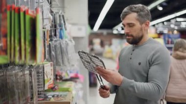 Yakışıklı sakallı adam ızgara ızgara süpermarkette seçmektir, kalite ve fiyat kontrol ve bakarak tutuyor. Barbekü ve alışveriş kavramı.