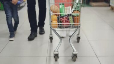 Mutlu genç aile alışveriş arabası süpermarket ile lezzetli yiyecek dolu iterek Tilt-up vurdu. Çocuk eğleniyor, ebeveyn gülümseyen ve etrafa.