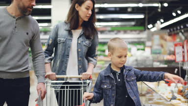 Küçük çocuk annesi ve babası, buzdolabı peynir alarak ve kokulu ile alışveriş sonra ailesine vermek, kaliteli ürün ve arabasına koyarak kontrol ediyor.