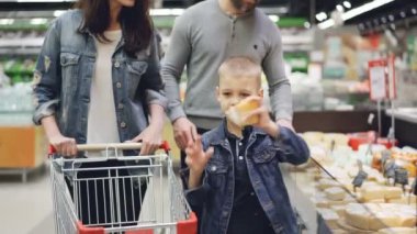 Anne, baba ve oğul mutlu aile süpermarket süt bölümünde peynir tercih ediyor, onlar adet buzdolabı ve onları kokulu, sonra arabasına koyarak üzerinden alıyor.