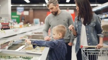 Küçük oğlan açılış dondurucu ve dondurulmuş sebze paketi alarak daha sonra ailesiyle birlikte süpermarkette alışveriş yaparken babasına veren var. İnsanlar ve salonu konsept.