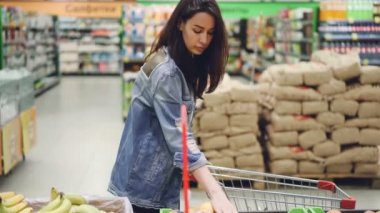 Güzel kadın mutlu müşteri meyve muz ve elma seçmek ve onları alışveriş sepeti koyarak süpermarkette satın alıyor. Sağlıklı yaşam tarzı ve mağaza konsepti.