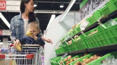 Genç aile anne ve oğlu bakkal meyve satın alıyor, armut ve kivi ve arabası içinde koyarak. Mutlu müşteriler ve süpermarket kavramı.