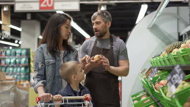 Deneyimli tezgâhtar neşeli genç aile anne ve çocuk, giving onları armut, elma ve ananas, mutlu müşteri gülerek ve gülümseyerek meyve satıyor.