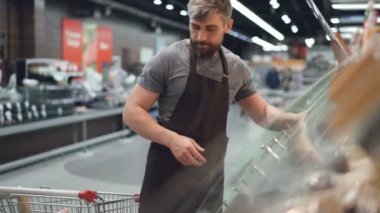 Yakışıklı işçi hipermarket, alışveriş sepeti ve onları raflarda fırın bölümünde kaplarda koyarak çörek alıyor. Satan yiyecek ve insan kavramı.