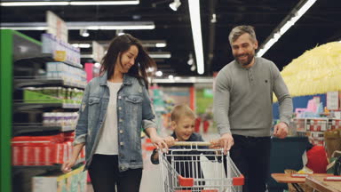 Ağır çekim mutlu aile babası, annesi ve gülümseyen ve gülerek süpermarket alışveriş sepeti ile aracılığıyla çalışan çocuk. Dükkanı ve insanlar kavramında eğleniyor.