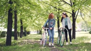Sportif genç kadın Parkı, Bisiklet ile gülümseyen ve konuşmaya yürüyor. Güzel doğa, ilginç konuşma ve neşeli insanlar kavramı.