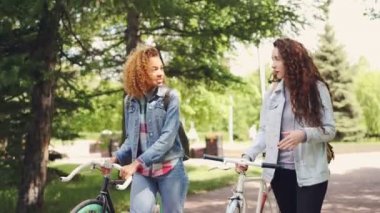 Güzel bir kadın güzel yeşil park bisiklet ve sırt çantaları ile yürürken ve konuşmaya neşeli turistler. Bisiklet Turizm, millennials ve insanlar kavramı.