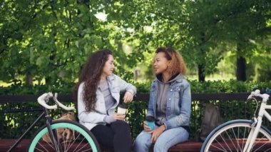 Çekici genç kadın Kafkas ve Afrikalı-Amerikalı sohbet ve park ve bisiklet sürme sonra dinlenme bankta otururken paket servisi olan restoran kahve içme.
