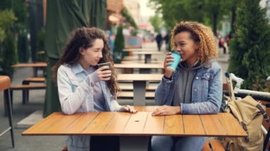 İki genç kadın kahve içme ve açık park, kafede masada oturan genç kadınlar konuşmaya eğleniyor ve gülüyor. Konuşma ve içecek konsepti.