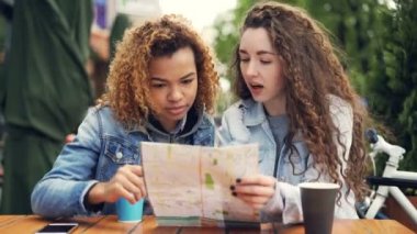 Heyecanlı kız turist şehir haritası kontrol ve sonra yabancı ülke Sokak kafede oturmuş gülüyor çevresinde arıyorum. Turizm, navigasyon ve insanlar kavramı.