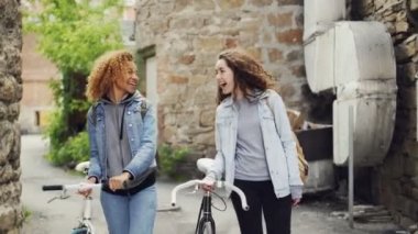 Heyecanlı Kafkas ve Afrikalı-Amerikalı kızlar turistler gülüyor ve ile yürüme tuğla duvarlı cadde boyunca eski binalar bisikletler. Turizm ve insanlar kavramı.