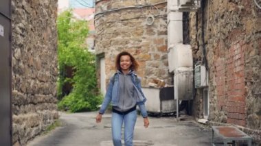 Kameraya bakarak sonra gülümseyerek ve saç dokunmadan poz dans ve yürüme çekici Afro-Amerikan Kız portresi. Mutluluk, millennials ve şehir hayat kavramı.